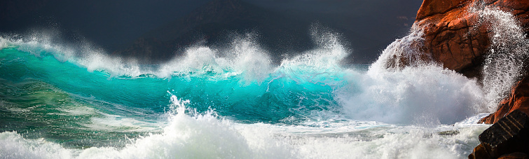 Large white waves of the sea break on the rocks. Breakwater near the small Village of Framura. La Spezia, Liguria, Italy, Europe. Mediterranean Sea.