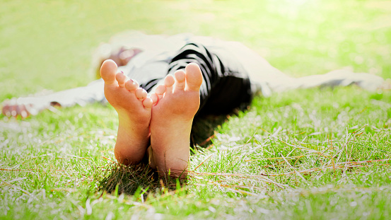 A young woman with bare feet laying down in a green grassy field.