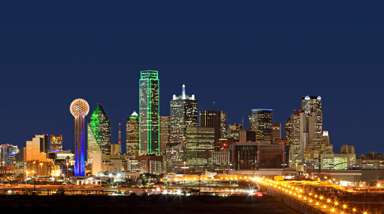 Wide-angle shot of Dallas, Texas business district showcasing skyscrapers glowing and lights glimmering at night.