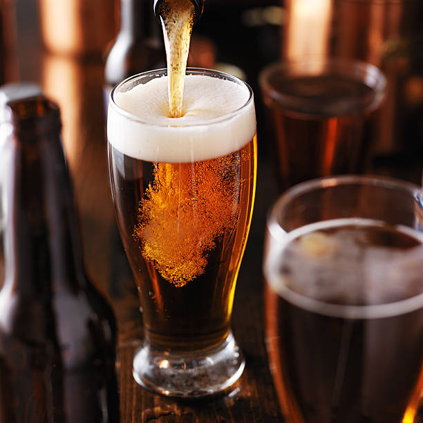 cerveza vertiendo en vidrio sobre mesa de madera - cerveza tipo ale fotografías e imágenes de stock