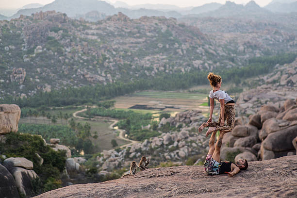 Hampi, India - January 14, 2014: A couple preforming acroyoga on a mountain looking over the landscape of Hampi at sunset.