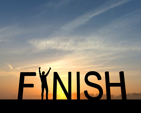 The finish win is silhouetted against an orange and blue sunset. The I in the word is made from a figure with their arms raised up in the air in a successful victory pose.