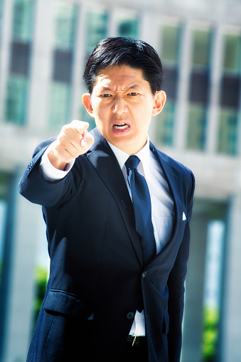 Furious Japanese businessman points at camera and threatens with an intense angry face. Photographed in Shinjuku, Tokyo, Japan.