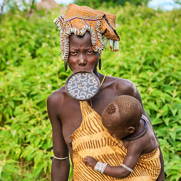 Woman from Mursi tribe holding her baby.  Mursi tribe are probably the last groups in Africa amongst whom it is still the norm for women to wear large pottery or wooden discs or ‘plates’ in their lower lips.http://bem.2be.pl/IS/ethiopia_380.jpg