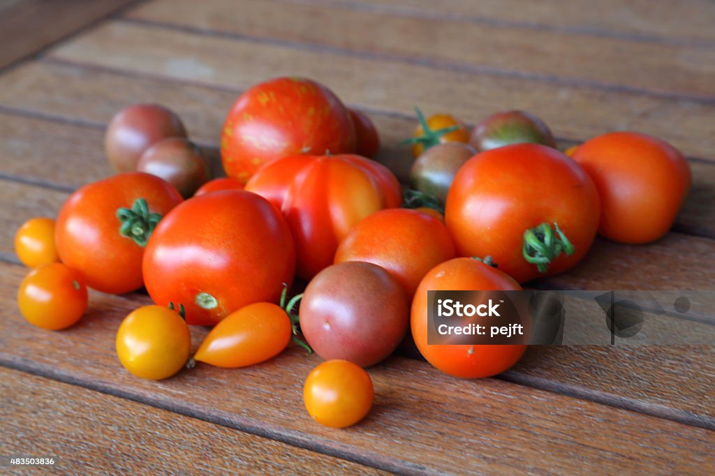 Fresh newly picked organic tomatoes on teak table Fresh newly picked organic tomatoes on teak table. I know they are organic - they are from my own garden and greenhouse 2015 Stock Photo