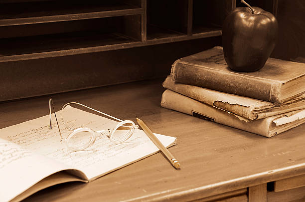 Vintage eye glasses on notebook on an old wooden teacher's desk with apple on books.