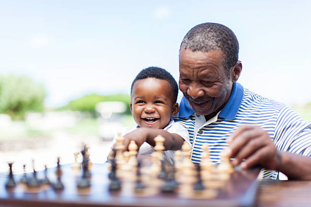 African grandfather playing chess with his grandson African grandfather sitting down with his grandson on his lap, teaching him how to play chess in Langebaan, Western Cape, South Africa senior chess stock pictures, royalty-free photos & images