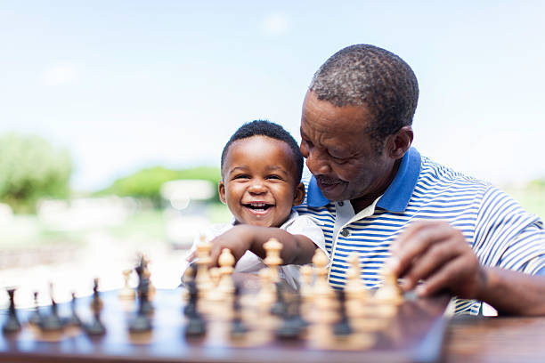 abuelo africano jugando al ajedrez con su nieto - juego de ajedrez fotografías e imágenes de stock