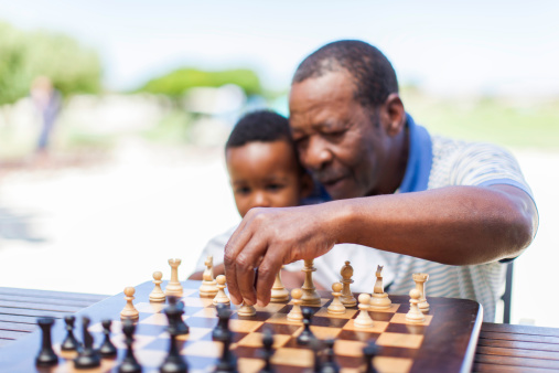 African grandfather sitting with his grandson on his lap teaching him how to play chess in Langebaan, Western Cape, South Africa