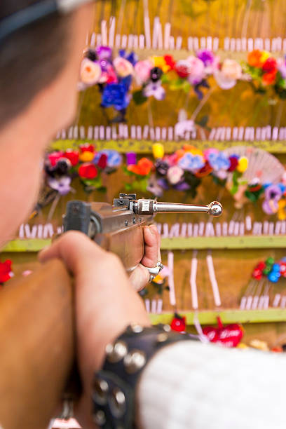 Young man at a amusement park doing some flower shooting at a gallery, a artificially rose for his girlfriend. Selective focus, unrecognizable person.