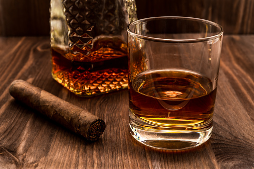 Decanter of whiskey and a glass with cuban cigar on a wooden table. Angle view