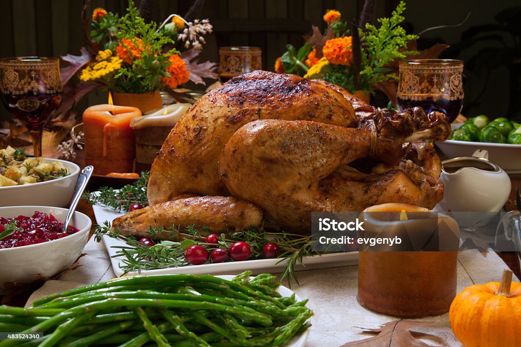 Rustic Thankgiving Dinner Roasted turkey garnished with cranberries on a rustic style table decorated with pumpkins, gourds, asparagus, Brussels sprouts, baked vegetables, pie, flowers, and candles. Roast Turkey Stock Photo