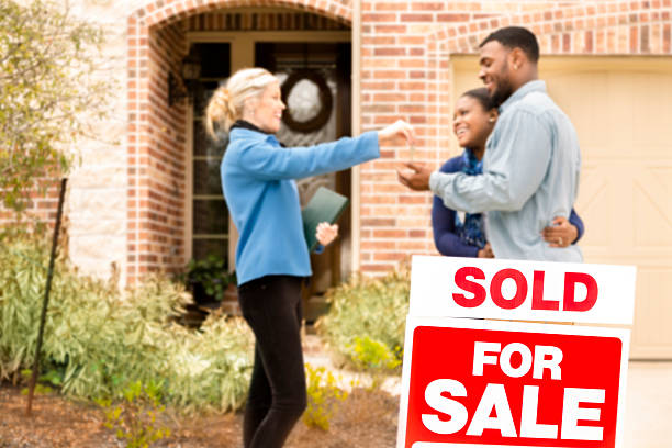 Real Estate: African descent couple buys home. Real Estate Agent gives key. African descent couple receives key from Real Estate Agent after purchasing a new home. 'Sold',  'For Sale' sign in foreground. Front yard view of this beautiful brick and stone home.  real estate sign photos stock pictures, royalty-free photos & images