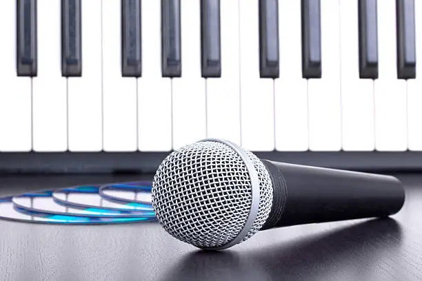 Photo of Microphone, cd disks and piano keyboard on black table