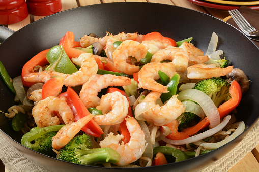 Closeup of shrimp stir fry in a wok with serving plates