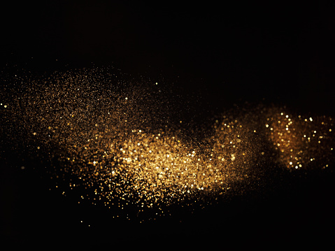 Golden glitter waving on black background. Studio shot using high speed technique, selective focus