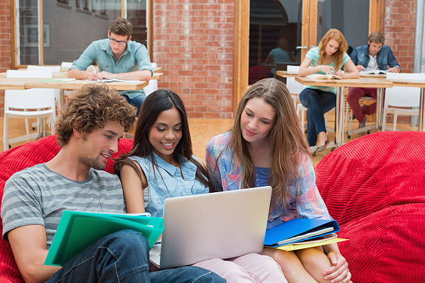 Happy students sitting on bean bags using laptop Happy students sitting on bean bags using laptop in college common room stock pictures, royalty-free photos & images