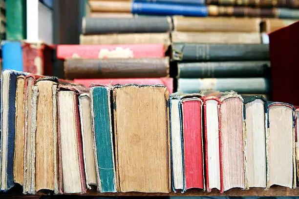 Row of old books on a bookshelf. Many of the books show lots of wear and damage from aging. 