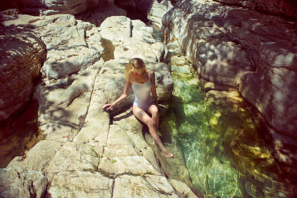 Woman sits and rest in the canyon. Her legs are in the water.