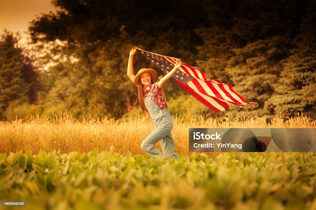 Americana Farm Girl with U.S. Flag on 4th of July Subject: A young farm girl running across the farm field with United States flag flying above her. Agricultural Field Stock Photo