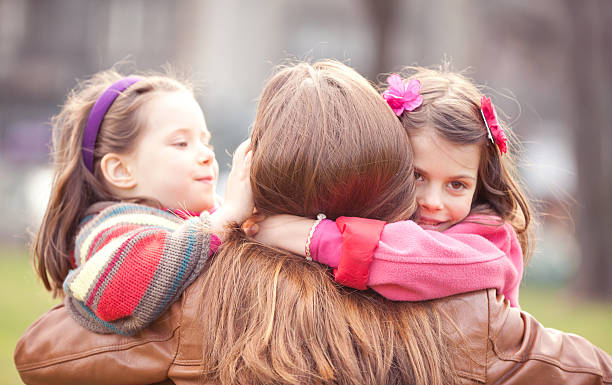 Two Happy Daughters Embracing their Mother Two Happy Daughters Embracing their Mother in the Spring Day . three way kiss stock pictures, royalty-free photos & images