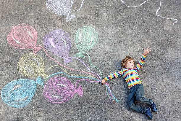 istock Kid boy having fun with colorful balloons drawing with chalks 483550250