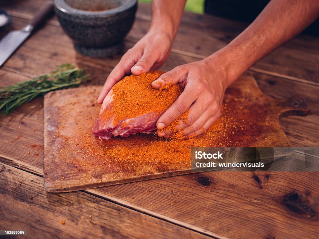 Person rubbing dry seasoning into a piece of raw pork Hands of a person rubbing some spicy dry seasoning into a fresh piece of raw pork on a wooden board Dry Stock Photo