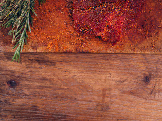 Overhead shot of a seasoned piece of fresh pork with some green herbs on a rustic table with wooden texture