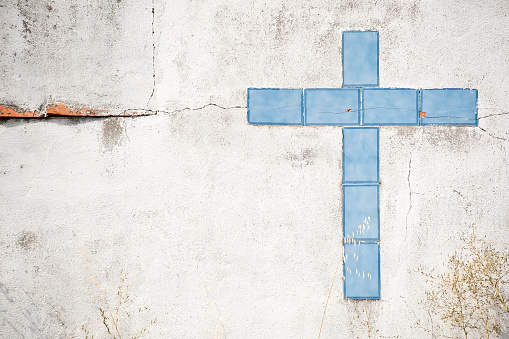 Cross built with broken blue tiles on a dirty wall