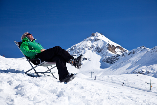 man sitting in a chair in snow, enjoying the winter sun