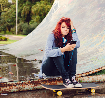 Teenage girl texting on smartphone with legs at skateboard