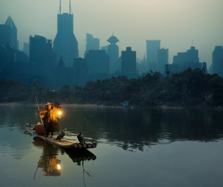 Cormorant fisherman in Shanghai against city background at dusk