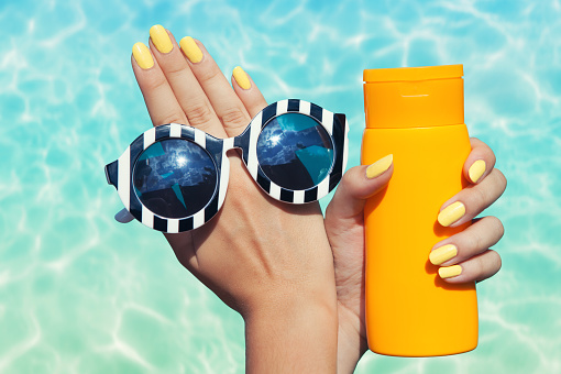 Summer fashion and beauty hand care concept, woman at the pool holding sunglasses and sunscreen lotion 