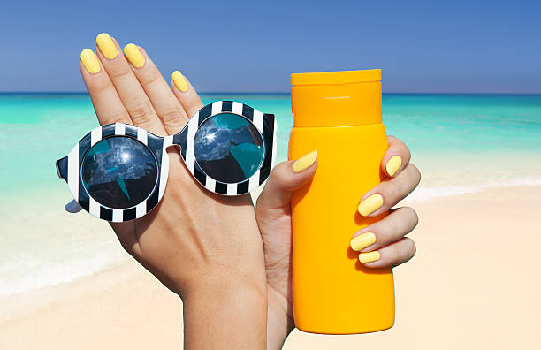 woman on the beach holding sunglasses and sunscreen lotion stock photo