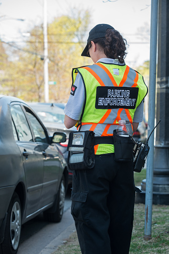 Halifax, Canada - May 8, 2013: A parking enforcement official with Securitas writes parking tickets for vehicles at expired street meters.