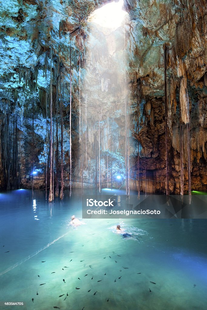 Cenote Dzitnup near Valladolid, Mexico couple (motion blur) swimming on a lovely cenote with transparent turquoise waters and large stalactites. ISO 1600 with slight noise Cenote Stock Photo