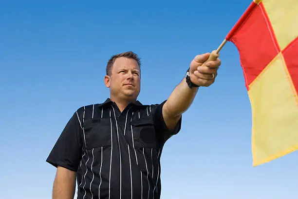 Low angle view of linesman showing penalty flag against clear blue sky