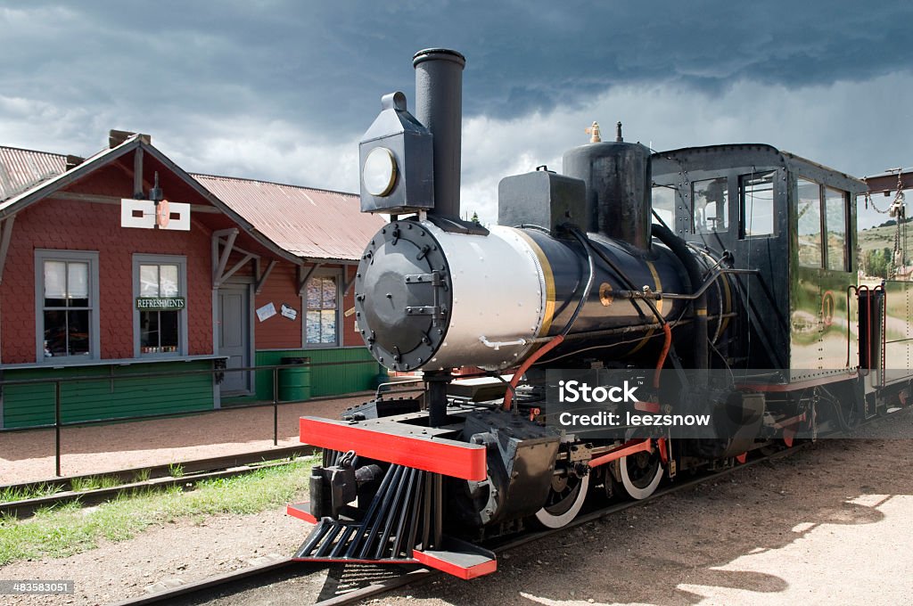 Narrow Gauge Steam Engine Train Old-fashioned steam engine in front of a rural depot in the high country of Colorado.  Taken under very moody skies of sun and looming dark clouds. Burning Stock Photo