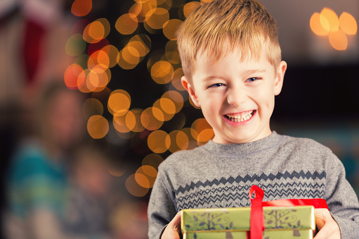 Excited young boy holding Christmas gift in front of tree
