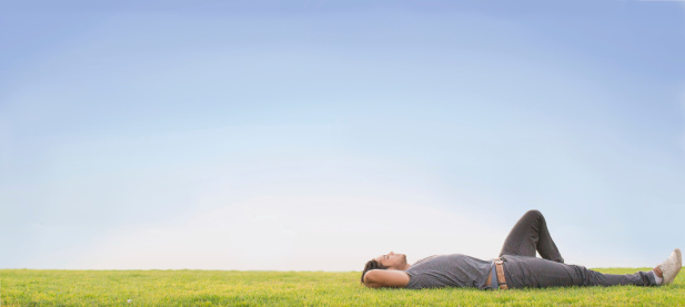 Relaxed young man laying on grass. Blue sky