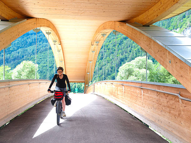 Front view of Biker riding over nridge on Drau cycle path by railroad near Aguntum ruins in Tirol, Austria. It is located in Valley of the Drava River near border of north Italy and Austria. One of nicest world Drau bike cycle paths (Grauradweg R1) goes from Toblach trough Innichen in Italy, Sillian, and Villach in Austria and to Maribor in Slovenia. It is cloudy day...