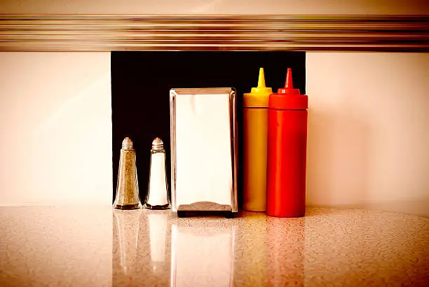 Sepia-processed image of a table in a roadside diner, with ketchup, mustard, napkins, salt, & pepper. Intentional vignette for effect. Adobe RGB color space.