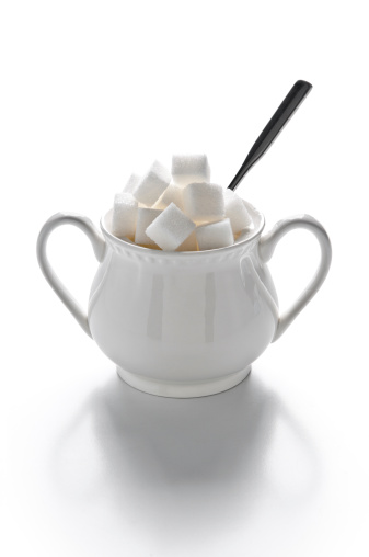 Sugar bowl full of sugar cubes and spoon, isolated on white background, studio shot.