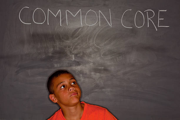 Elementary age boy in front of chalkboard with "common core" stock photo