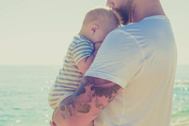 close-up de pai segurando bebê filho na praia - tattoo father family son imagens e fotografias de stock