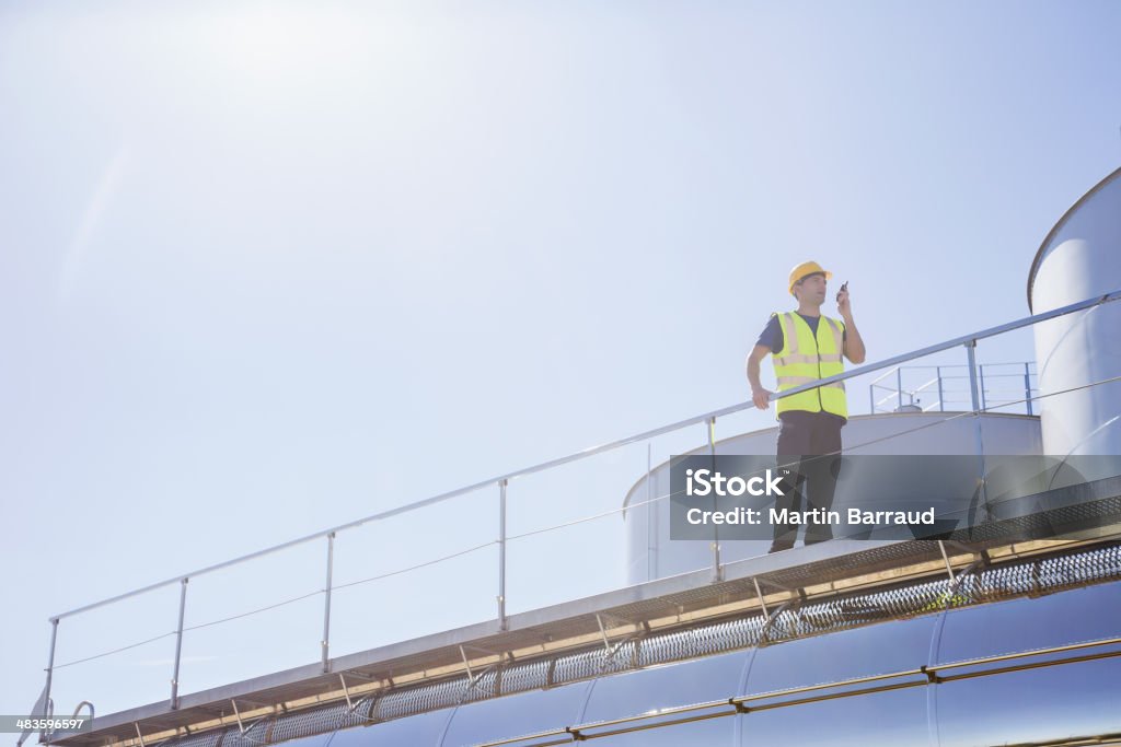 Worker using walkie-talkie on platform next to silage storage towers  Agriculture Stock Photo