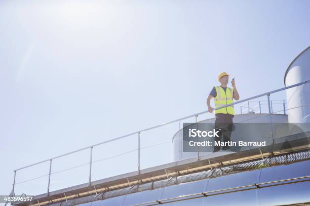 Worker Using Walkietalkie On Platform Next To Silage Storage Towers Stock Photo - Download Image Now