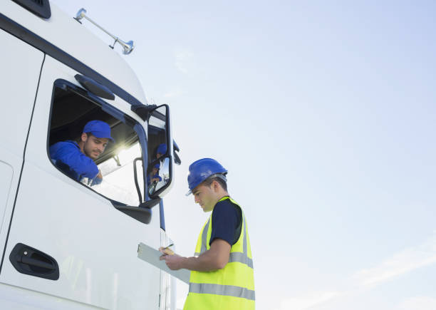Worker with clipboard talking to truck driver stock photo