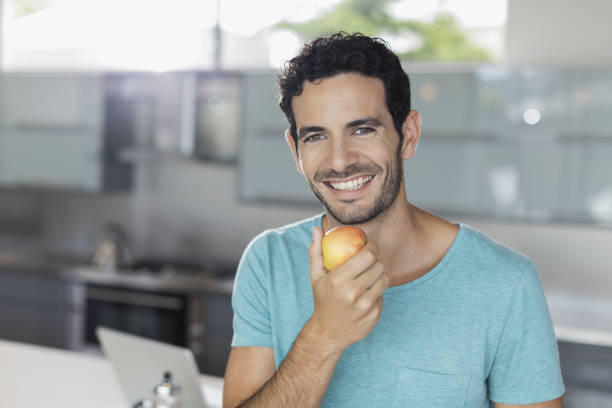 istock Portrait of smiling man eating apple in kitchen 483599075