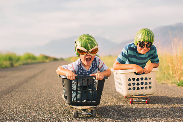 Young Boys Racing Wearing Watermelon Helmets A young boy races his brother in a makeshift go-cart while wearing watermelon helmets and goggles. He is excited as he is winning the race. nerd kid stock pictures, royalty-free photos & images